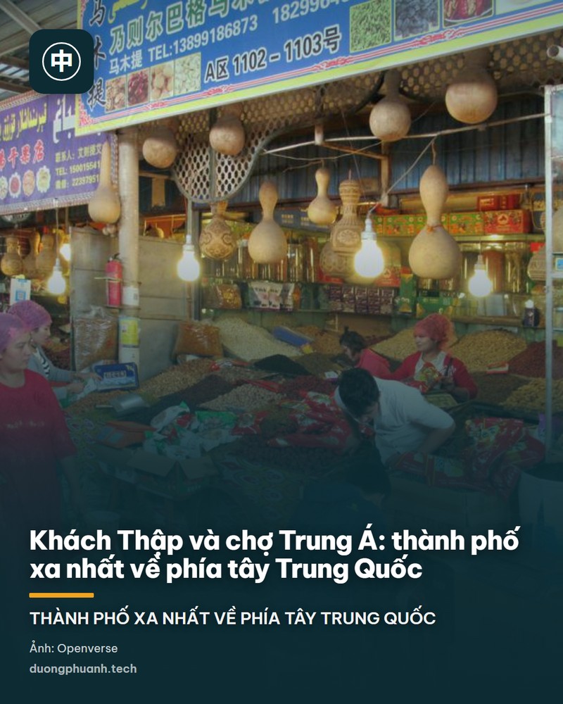 Một sạp hàng trong chợ Khách Thập: hai người phụ nữ Uyghur mặc váy lụa hồng và đỏ đi ngang, trước mặt là các khay hạt và quả khô đầy ắp, những quả bầu khô treo thành dãy trên trần sạp, biển hiệu viết song ngữ chữ Trung và chữ Uyghur, bóng đèn tròn treo thấp chiếu sáng quầy hàng.