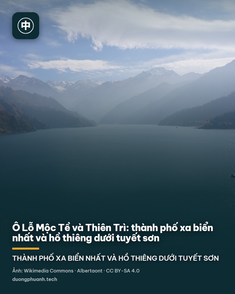 Hồ Thiên Trì ở Tân Cương nhìn từ bờ: mặt nước xanh thẫm phẳng lặng trải rộng giữa những rặng vân sam cao thẳng đứng ở tiền cảnh, phía sau là sườn núi đá nâu vàng có vài vệt tuyết trắng, bầu trời xanh nhạt có mây mỏng; ở góc trái dưới, một người cưỡi ngựa nâu đang đi trên bãi cỏ khô ven bờ.