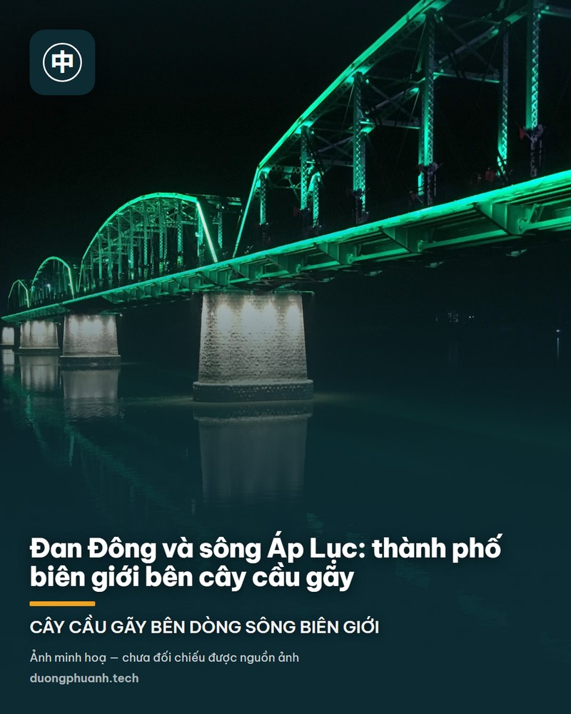 Ảnh chụp trên mặt cầu gãy sông Áp Lục ở Đan Đông: lối đi bộ lát đá dẫn vào khung dàn thép xanh sẫm, phía trên treo tấm biển gỗ khắc chữ Hán lớn, bên trái là bảng đá ghi tên cầu và một cột đèn, phía xa thấy nhịp cầu cũ bắc ngang mặt sông xám dưới trời nhiều mây