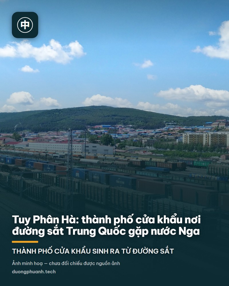 Toàn cảnh bãi đường sắt Tuy Phân Hà nhìn từ trên cao: hàng chục đoàn tàu hàng xếp dọc theo các đường ray song song, nhiều toa container xanh đỏ và toa chở gỗ, phía sau là dãy đồi phủ rừng xanh và những dãy nhà thấp của thành phố dưới bầu trời xanh nhiều mây trắng