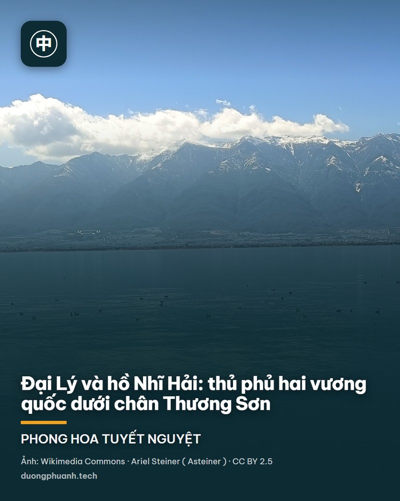 Toàn cảnh hồ Nhĩ Hải nhìn từ trên cao: mặt nước phẳng lặng màu xanh thép trải dài, phản chiếu mây trắng. Phía sau là dãy Thương Sơn chạy ngang tầm mắt với những đỉnh núi phủ tuyết trắng nổi bật trên nền trời xanh; một dải đô thị mảnh chạy dọc chân núi ven bờ hồ, vài chiếc thuyền nhỏ ở giữa hồ.