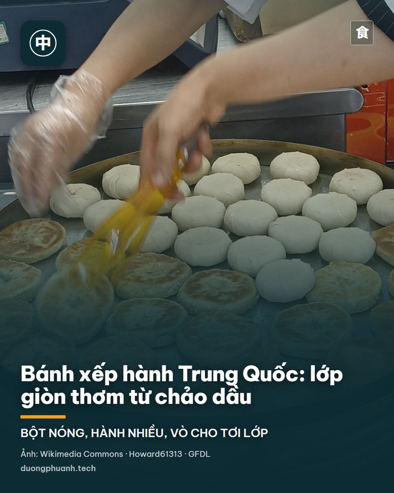 Cận cảnh một chiếc bánh xếp hành chiên vàng trên đĩa trắng, thấy rõ từng lớp bột tơi tách ra và những sợi hành lá xanh nằm giữa các lớp