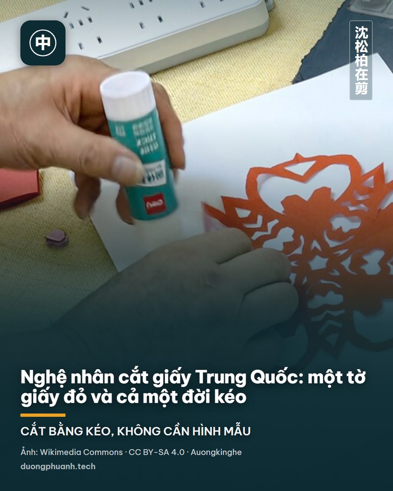 Nghệ nhân cắt giấy Trung Quốc cúi người bên bàn, tay phải cầm kéo cắt liền một mạch một mẫu giấy, phía sau là màn chiếu ghi các bước hướng dẫn và một lớp học trò đang ngồi cắt giấy theo