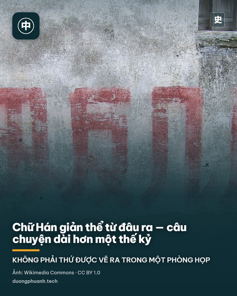 Tấm biển gỗ cắm bên vệ đường thành phố, viết tay hai chữ Hán màu đỏ theo lối giản thể đợt hai, bên cạnh gốc cây và cột tiêu giao thông